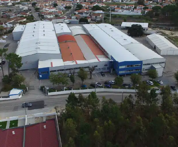 Black sedan parked by a glass building with trees and hills in the background.